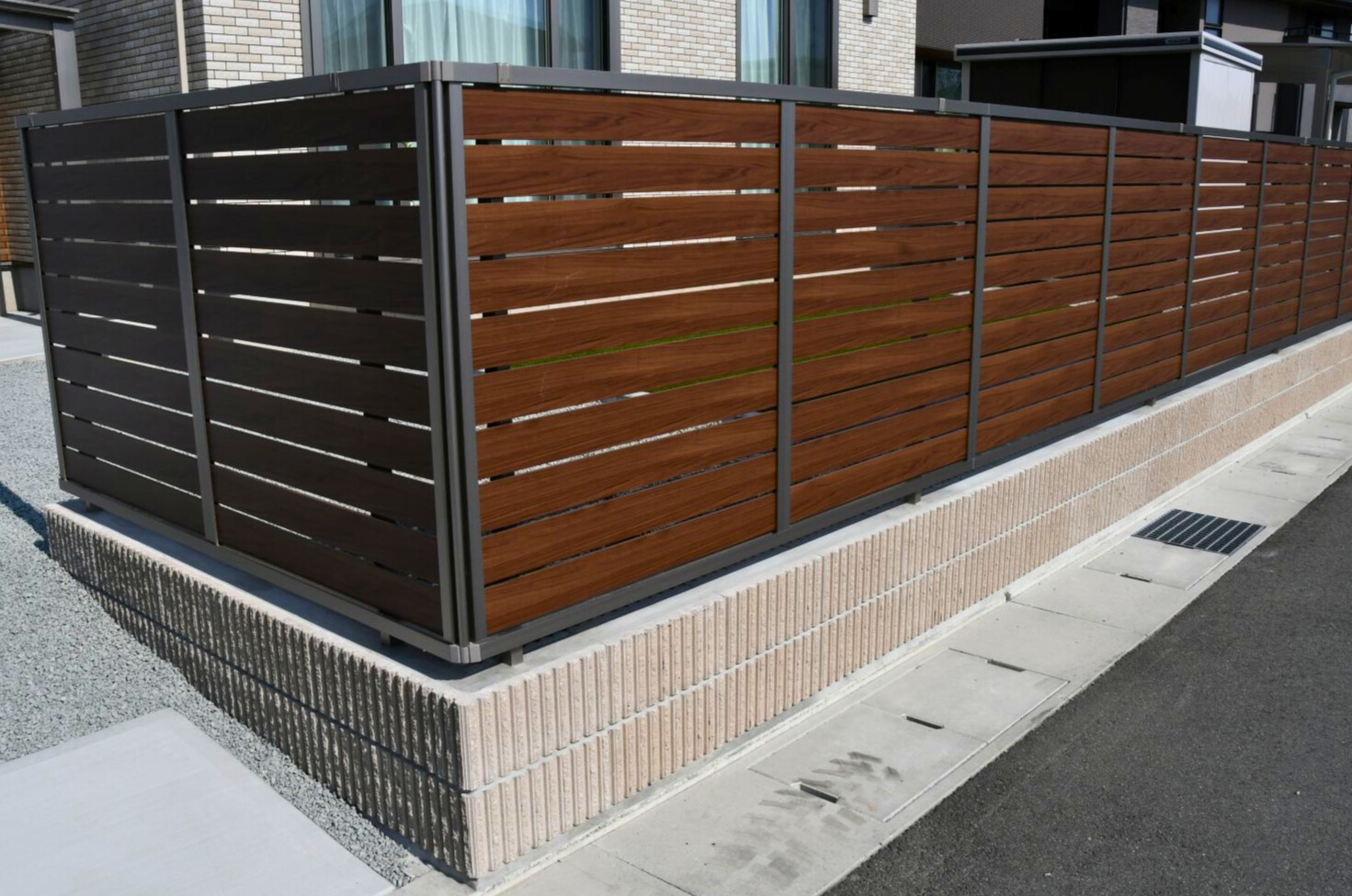 2段積みのブロック上に木目調のアルミフェンス（横格子）を設置。
